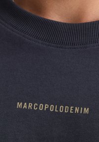 Granatowy sweatshirt z prążkowanym dekoltem, z napisem "MARCOPOLODENIM" złotymi literami na przodzie. Gładka faktura materiału.