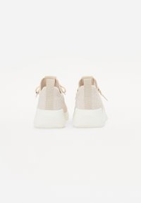 Baskets de sport beige avec une tige en tissu texturé et une semelle extérieure blanche lisse et moulée. Comprend une languette en tissu au talon et des lacets pour un ajustement sécurisé.