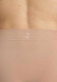Nude seamless stretch fabric with a wide waistband, featuring subtle branding. Smooth texture and form-fitting design.