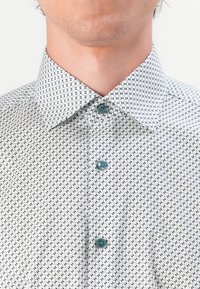 Button-up shirt with a light background, featuring a navy geometric pattern, a pointed collar, and teal buttons.
