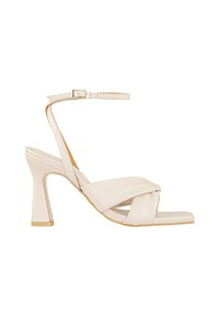 Sandal de tacón alto beige con diseño de tiras cruzadas, correa en el tobillo, punta abierta y un tacón ligeramente cónico con un acento dorado en la base.