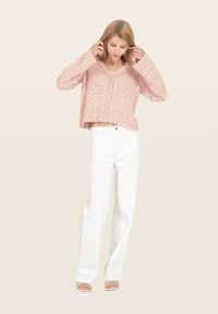 Pull en tricot rose clair avec décolleté en V, manches longues et motif ajouré, associé à un jean blanc taille haute et des sandales.