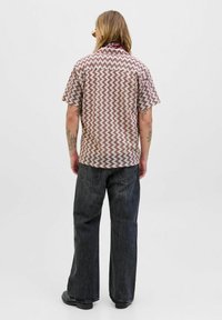 Camicetta a maniche corte con motivo a zigzag rosso e crema; vestibilità rilassata, colletto a scialle, indossata con jeans scuri e scarpe nere.