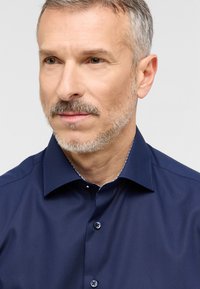 Donkerblauwe button-up shirt met een gestructureerde kraag, voorzien van een contrasterende patroonrand. Gladde textuur, getailleerde pasvorm en standaard manchetten.