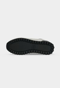 Semelle d'une basket gris clair avec une semelle extérieure noire profonde rainurée et le nom de la marque embossé près du centre de la semelle.