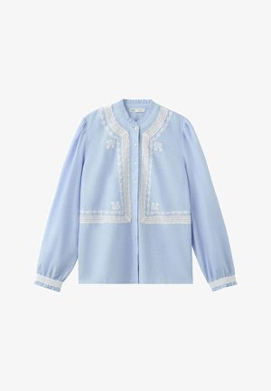 Blouse bleu clair à manches longues avec bordure en dentelle blanche et broderie florale sur le devant, fermeture à boutons, et poignets élastiques avec détail en dentelle.