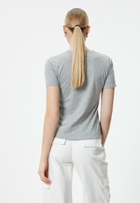 Grå t-shirt med korte ærmer og tætsiddende design, lavet af et blødt materiale, sammen med hvide cargobukser. Minimalistisk og alsidig stil.