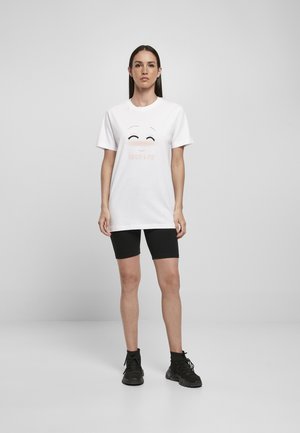 T-shirt bianca in cotone con un design di un volto sorridente, che presenta il testo "BUONA VITA" in rosa chiaro. Abbinarla a pantaloni corti neri e scarpe nere.