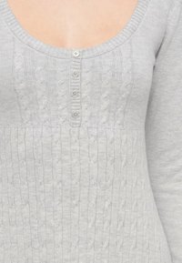 Ανοιχτό γκρι πλεκτό πουλόβερ με στρογγυλή λαιμόκοψη, με σχέδιο πλέξης καλωδίου και πέντε κουμπιά στο κέντρο. Μαλακή υφή.