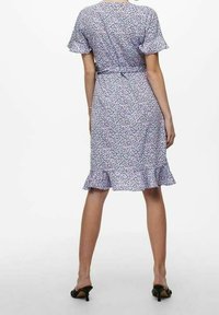 Lila Blumenmusterkleid mit kurzen Rüschensäumen, Gürtel in der Taille und ausgestellt gestaltetem Saum. Leichte Stoffqualität mit subtiler Struktur, knielang.