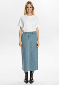 Denim garais svārki ar augstu jostasvietu, gaiši zilā krāsā, ar jostu cilpām un sānu šuvēm, apvienoti ar vienkāršu baltu T-kreklu un melniem zābakiem.