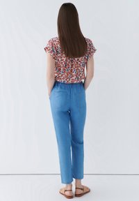 Blommig blus med en samlad halsringning, i kombination med ljusblå byxor med elastisk midja och bakfickor. Bruna sandaler.