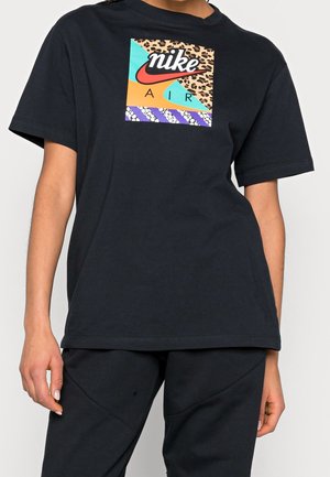 Personne portant un t-shirt noir Nike Air avec un logo carré multicolore comprenant un motif léopard, des motifs et un texte en gras sur la poitrine.