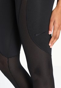 Czarne legginsy sportowe z teksturowanym wzorem małych paneli siatkowych oraz subtelnym logo Nike z boku. Gładki materiał i dopasowany krój.