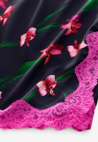 Zwarte stof met roze bloemenprint en groene bladeren; afgewerkt met een gedetailleerde roze kantafwerking. Een kleine gouden charme is zichtbaar nabij het kant.