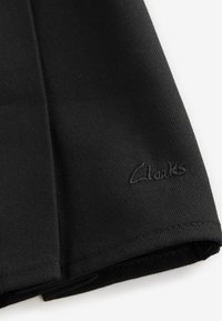 Sort stofsko med en glat tekstur, der har en diskret broderet "Clarks"-logo på siden. Klassisk design og struktureret form.