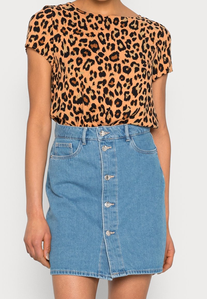 Personne portant un haut à manches courtes imprimé léopard rentré dans une jupe en denim bleue taille haute avec boutons devant.