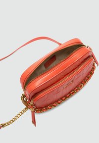 Rote Leder-Crossbody-Tasche mit goldenen Kettenakzenten, die zwei mit Reißverschlüssen versehenen Fächer und eine strukturierte Oberfläche aufweist.