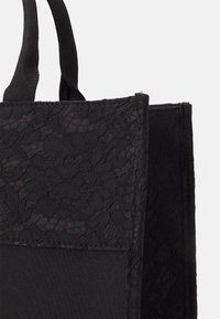 Borsa a tracolla nera con dettagli in pizzo testurizzato su un lato, tessuto liscio dall'altro e manici in tessuto corti.