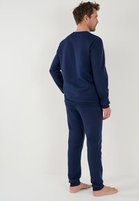 Donkerblauw sweatshirt en sweatpants set in zachte stof, met een ronde halslijn en geribde manchetten, gedragen op blote voeten, gezien vanachter.