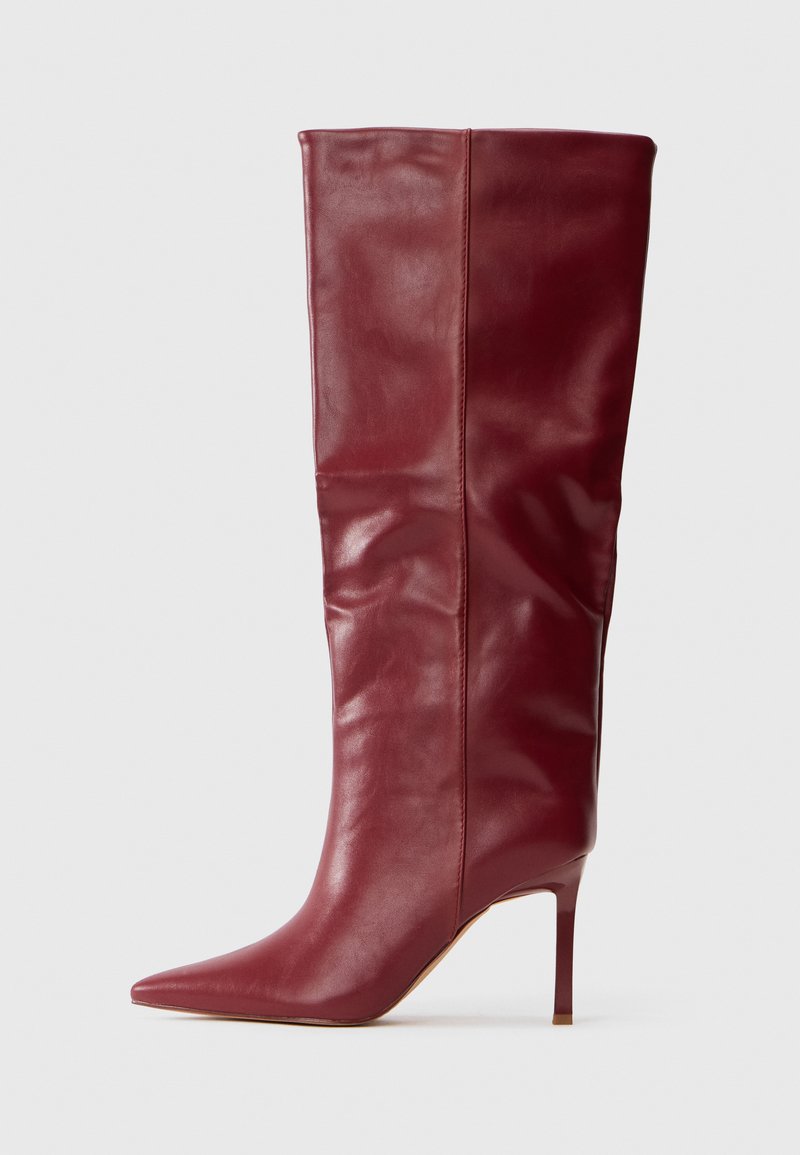 Bota alta de cuero burdeos con puntera puntiaguda y tacón delgado alto, acabado suave y ligeras arrugas naturales.