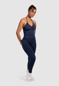 Granatowy komplet odzieży sportowej z dopasowanym topem na ramiączkach z marszczeniami i regulowanymi paskami, połączony z legginsami z wysokim stanem. Gładka tekstura.