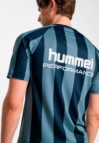 Koszulka sportowa w granatowo-turkusowe paski z krótkimi rękawami, wykonana z teksturowanej tkaniny, z logo "hummel PERFORMANCE" na plecach.