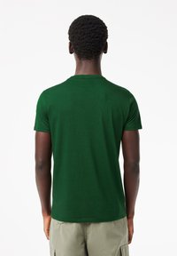 Vihreä lyhythihainen t-paita, joka on valmistettu puuvillasta ja jossa on pyöreä kaula-aukko sekä sileä pinta. Takakatsauksessa on yksinkertainen muotoilu ilman graafisia elementtejä.