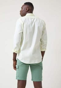 Camisa de manga larga verde claro con cuello abotonado, combinada con pantalones cortos de cargo verde menta que tienen bolsillos laterales y un corte casual.