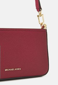 Borsa a mano in pelle bordeaux con superficie testurizzata, hardware dorato e dettaglio del logo. Presenta una tracolla staccabile per una maggiore versatilità.