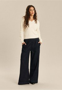 Crème v-hals trui gecombineerd met donkerblauwe wijde broek met een elastische tailleband en zijzakken. Eenvoudig en casual ontwerp.