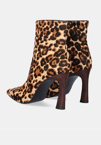 Par de botas de tobillo con estampado de leopardo, con puntas afiladas y tacones altos de madera en un fondo blanco.