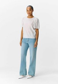 Witte korte mouwen top met bloemenborduursel, gecombineerd met lichtblauwe, uitlopende jeans en witte puntige hakken.