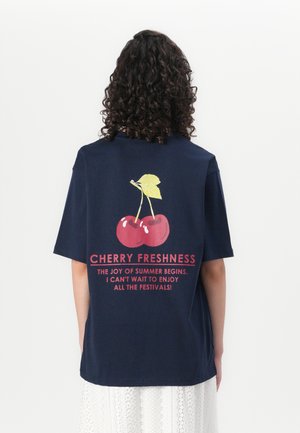 Marineblå oversized t-skjorte med kirsebærgrafikk og tekst i rødt. Bomullsstoffet har en jevn tekstur og en avslappet passform.