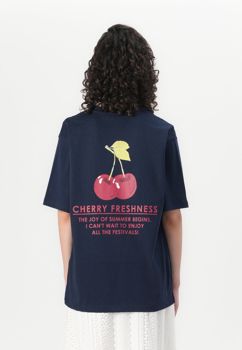 T-shirt overdimensionato blu navy con grafica di ciliegie e testo rosso. Il tessuto in cotone ha una texture liscia e una vestibilità comoda.