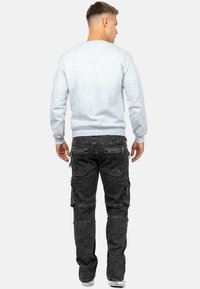 Felpa grigia chiara con maniche lunghe e polsini a costine, abbinata a jeans cargo neri con molteplici tasche e cerniere.