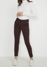 Bordó slim fit kalhoty s hladkou texturou, bočními kapsami a zúženým střihem, spárované s bílým tunikovým svetrem s dlouhým rukávem.