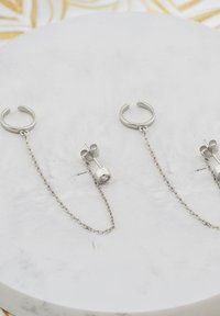 Silver hoops örhängen med en kedjelänkdesign. Varje örhänge har en cylindrisk hänge med en klar sten, vilket framhäver en minimalistisk estetik.