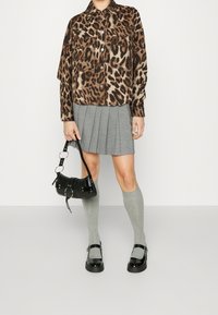 Leopard-print oversized shirt, gray pleated skirt, knee-high gray socks, black patent flats, and a small black bag with silver accents.