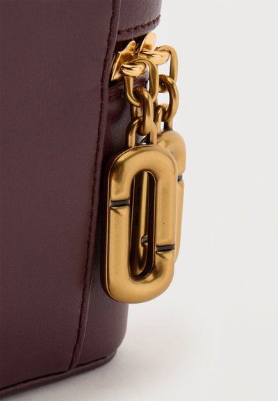 Gros plan d’un coin d’un sac en cuir marron avec deux grandes fermoirs en chaîne dorée reliées.