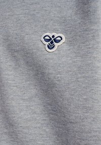 Grå sweatshirt tyg med en mjuk textur; har en liten, broderad bi-logotyp i marinblått och vitt på vänster sida.