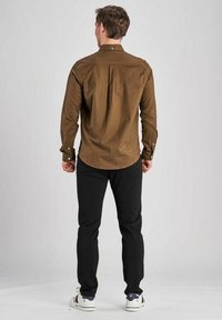 Cămașă maro cu mânecă lungă și butoane, cu o croială lejeră, asortată cu pantaloni negri și adidași albi. Țesătura pare texturată.