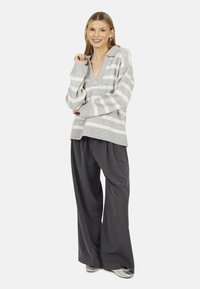 Maglione a righe grigie e bianche con scollo a V e orlo a coste, abbinato a pantaloni grigi plissettati a vita alta e scarpe argentate.