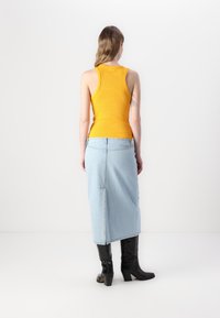 Débardeur à côtes jaune associé à une jupe en denim bleu clair, avec une fente centrale et des bottes noires jusqu'aux genoux. Design lisse et ajusté.