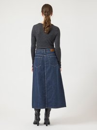 Denim maksiskjørt i mørk blå farge, med høy midje, baklommer og rett snitt. Brukt med en tettsittende svart langermet topp og svarte støvler.