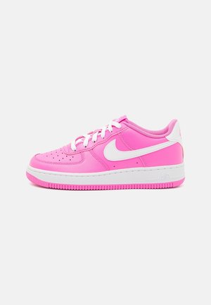 Basket basse rose vif avec le swoosh blanc de Nike, lacets blancs et semelle blanche avec semelle extérieure rose sur fond clair uni.