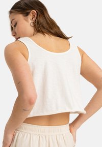 White cropped tank top made of soft, textured fabric, featuring a wide round neckline and a relaxed fit, paired with beige elastic-waist shorts.