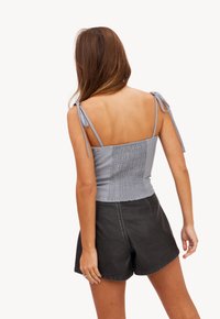 Grijze crop top met gesmokte achterkant, verstelbare schouderbandjes en een getailleerd ontwerp. In combinatie met zwarte high-waisted shorts.