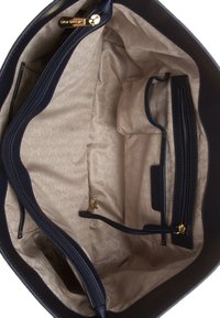 Interieur van een navy leren handtas met een beige, patroonvoering, meerdere zakken en goudkleurige ritsen.
