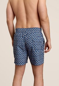 Blauwe zwembroek met een geometrisch patroon in lichtroze en wit. Elastische tailleband, zijzakken en een lichte stof.